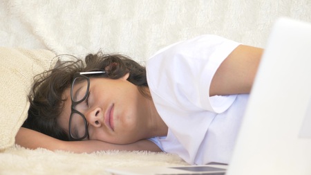 cute boy teenager wearing glasses sleeps on couch next to laptop.の写真素材