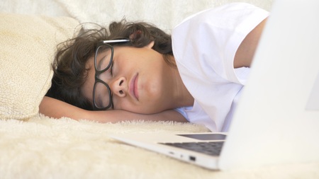 cute boy teenager wearing glasses sleeps on couch next to laptop.の写真素材