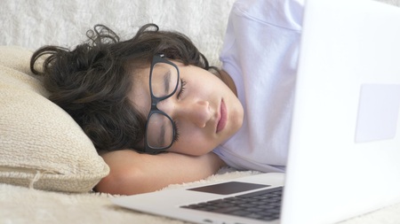cute boy teenager wearing glasses sleeps on couch next to laptop.の写真素材