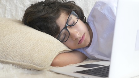 cute boy teenager wearing glasses sleeps on couch next to laptop.の写真素材