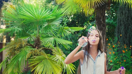girl teen brunette blowing soap bubbles against a tropical park background.の写真素材