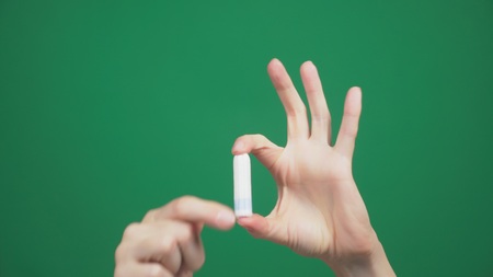 close-up, female hands hold a tampon on a green background