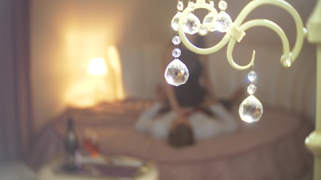 Focus on the round crystals from the lamp. Ardent loving couple is sitting on bed and hugging with passion on background. Romantic date concept. blur.の写真素材