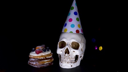 cake and skull in a festive cap on a black background. candy, slow-motion shooting