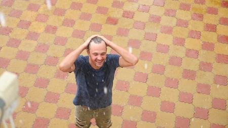 A young handsome guy rejoices in the rain by lifting his hands up and washing rain waterの写真素材