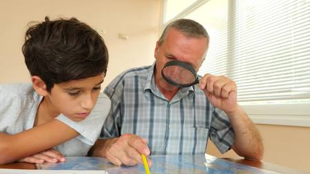 Senior man looking at the map with grandson through the magnifying glass of the house in the office,...