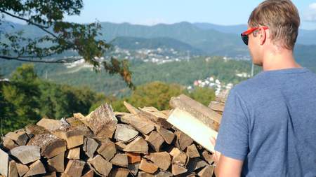 the man is picking up firewood. Stack of Wood for a Frosty Winter, for lighting a fireplace in a chalet. against the background of the mountains.の写真素材