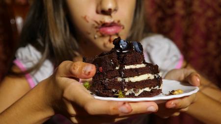 a little girl eats cake with fresh berries. her face in chocolate, she is happyの写真素材