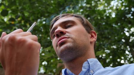 unhappy young man smoking a cigarette outdoors under a tree. close-up. smoky fire. the boy smokes. human lipsの写真素材