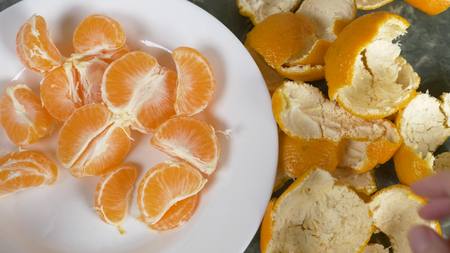 The hands of different people take tangerines from a plate on the table.の写真素材