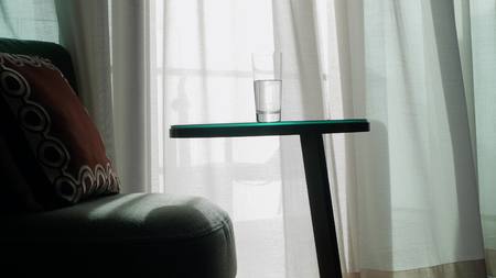 A cozy armchair and a table with a glass of water against the background of the Transparent curtain on the window, gently driven by the wind. Sunbeam.の写真素材