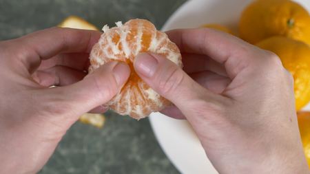 womens hands peel the peel of mandarins, mandarin slices are piled in a bowl.