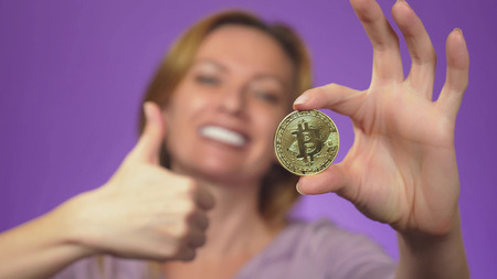 a young woman with a white-toothed smile in the background is blurry, holds in her hand a bitcoin gold coin. bitcoin sharpness. color backgroundの写真素材