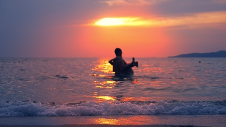 silhouettes, couple, man and woman out of the sea holding hands against the background of seascape, red dramatic sunset on the sea. the sun colors the sea red.の写真素材
