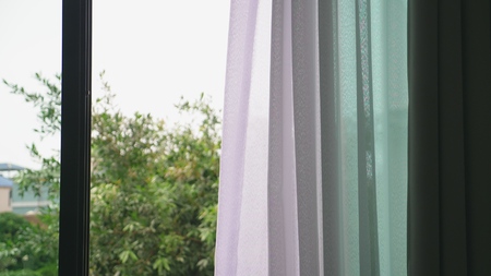 Transparent window curtain, gently moved by the wind. outside the window you can see the green...