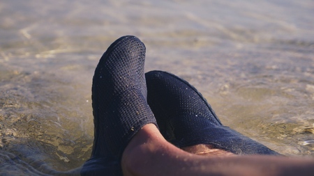 close-up of female legs in black shoes for swimming on the background of transparent sea water