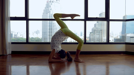 slim young girl stretching in front of a large panoramic window overlooking the skyscrapers