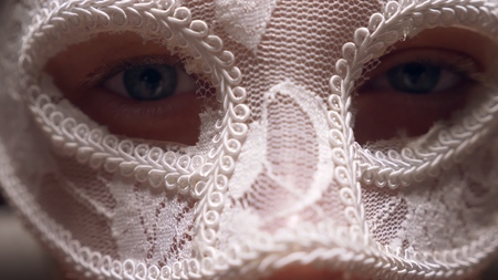 white lace mask on a womans face, close-up. blue eyes look into the camera through the mask on his face.の写真素材