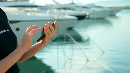 female hand holds smartphone on blurred background of port with yachtsの写真素材