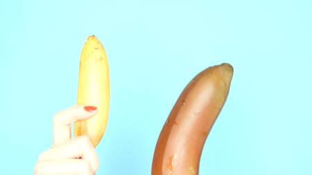 female hands with red nails are holding a red banana and a yellow banana on a blue background