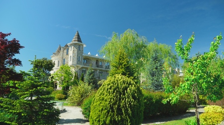 luxurious hotel in Victorian style, immersed in beautiful trees and bushes. roofs with spiers on a...