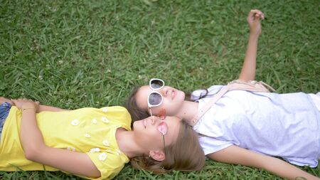 summer vacation concept. View from above. Two cute cheerful teen girls in sunglasses lying on the green lawn together. Summer sunny day.の写真素材