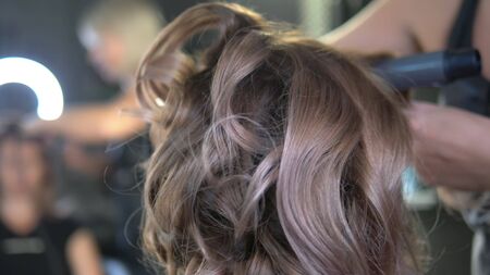 close-up. Professional hairdresser using curling iron. Hair curls in salon,
