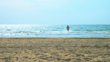 young man runs on a sandy beach at sea.