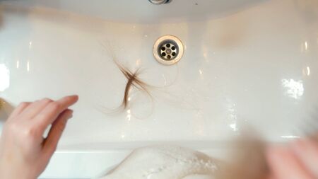 alopecia, baldness. the blonde combs her hair in the bathroom and a tuft of hair remains in the sink. copy space.の写真素材