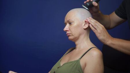 man shaves a bald woman with an electric razor on a blue background. chemotherapy effects concept.の写真素材