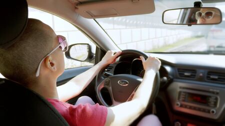beautiful bald woman in sun-protection glasses driving a car in traffic.