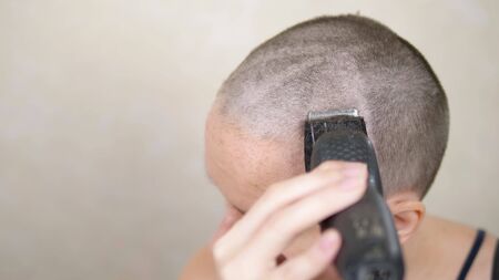 bald woman shaves her head with an electric razor. close-up, copy spaceの写真素材