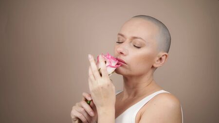 Beautiful smiling bald girl sniffs a pink rose. beige background, copy spaceの写真素材