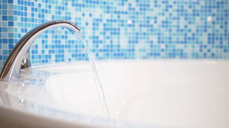 close-up. water flows from a luxurious water tap into a large modern bathtub against a blue mosaic wallの写真素材