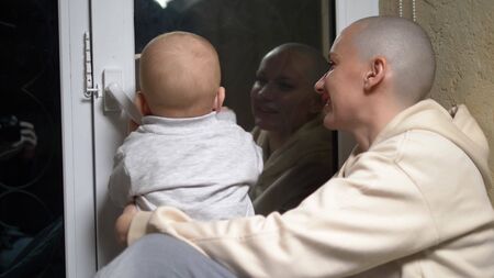 bald woman and baby sit together at the window in the evening.close-upの写真素材