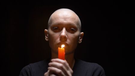 Portrait of a bald woman with a candle on a black background. copy spaceの写真素材