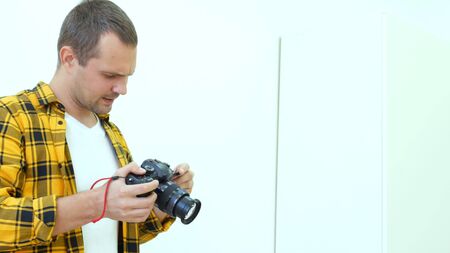 Handsome young man in a yellow checkered shirt, professional photographer holding a camera takes...