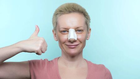 a woman with a bandage on her nose after rhinoplasty shows an ok sign