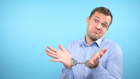 a man looks into the camera and shows the handcuffs. blue background