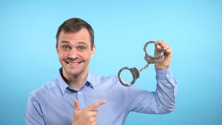 a man looks into the camera and shows the handcuffs. blue background