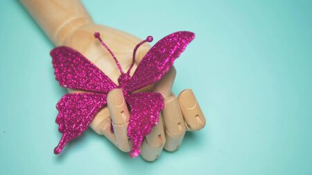 wooden hand holding an artificial butterfly. blue background