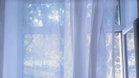 Transparent window blind with wrought iron grilles gently moved by the wind