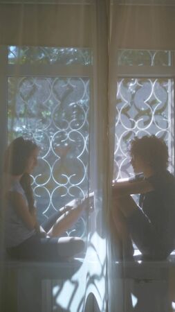 vertically, teenage brother and sister are sitting on the windowsill