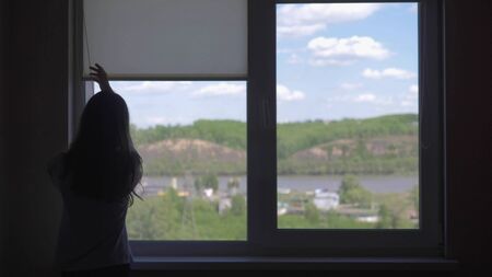 silhouette. the girl opens the blinds, the view from the window on the skyの写真素材