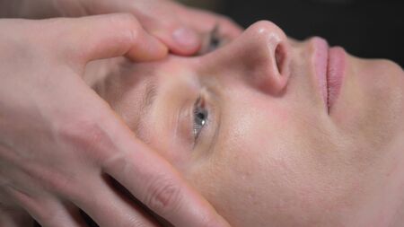 masseur gives woman anti-aging facial massage in spa