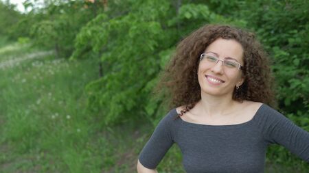 beautiful girl in glasses with curly hair walks in the park on a background of trees