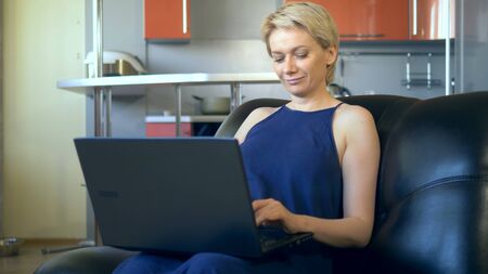 beautiful young woman uses laptop sitting in a chair in the kitchenの写真素材