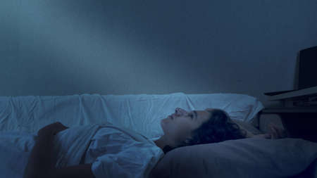 teenage boy suffering from insomnia lying in bed at nightの写真素材