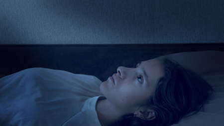 portrait of a teenage girl suffering from insomnia lying in bed at nightの写真素材