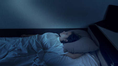 portrait of a teenage girl suffering from insomnia lying in bed at nightの写真素材
